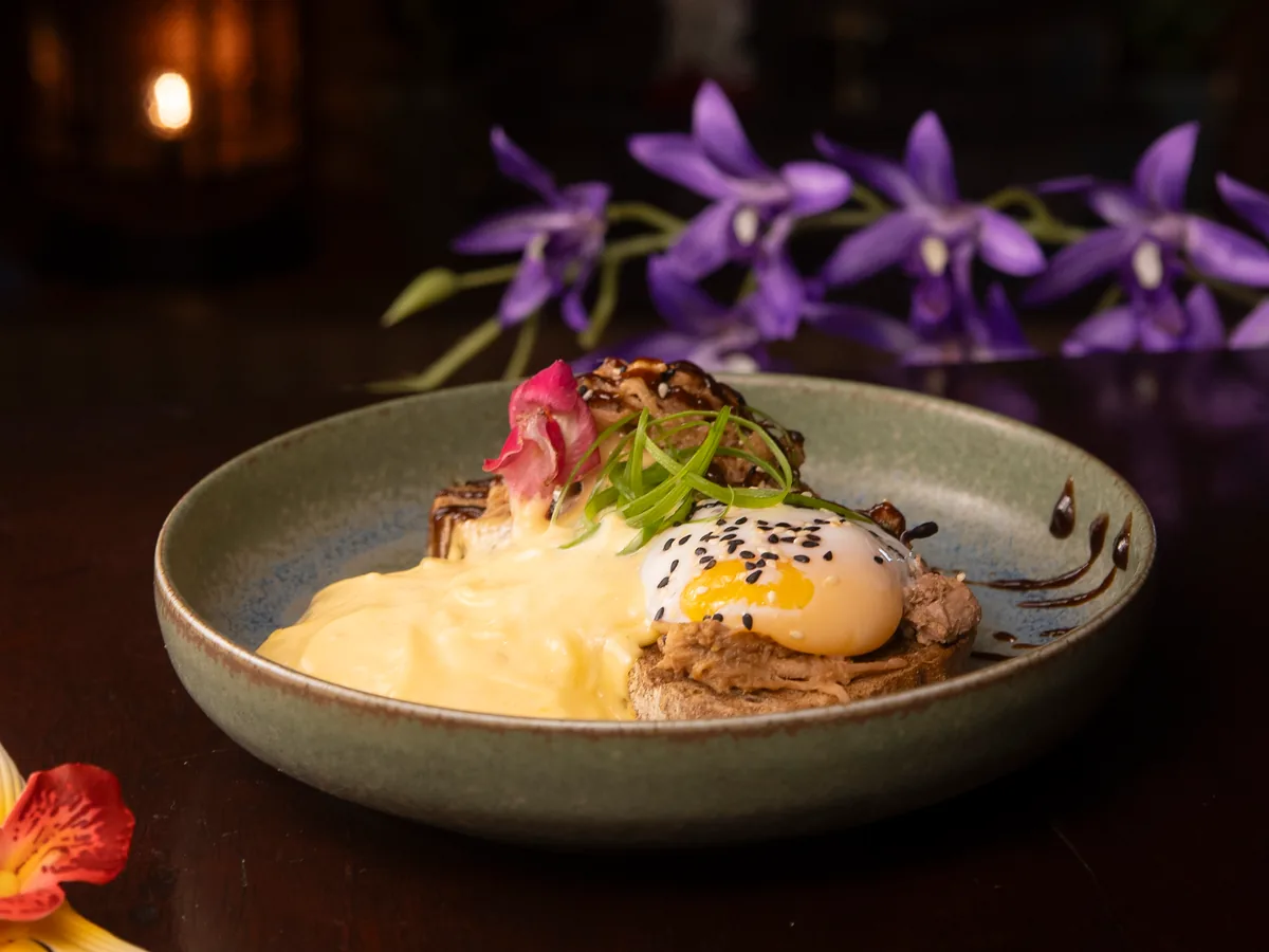 Huevos Benedict con orquídeas moradas y un farolillo encendido al fondo