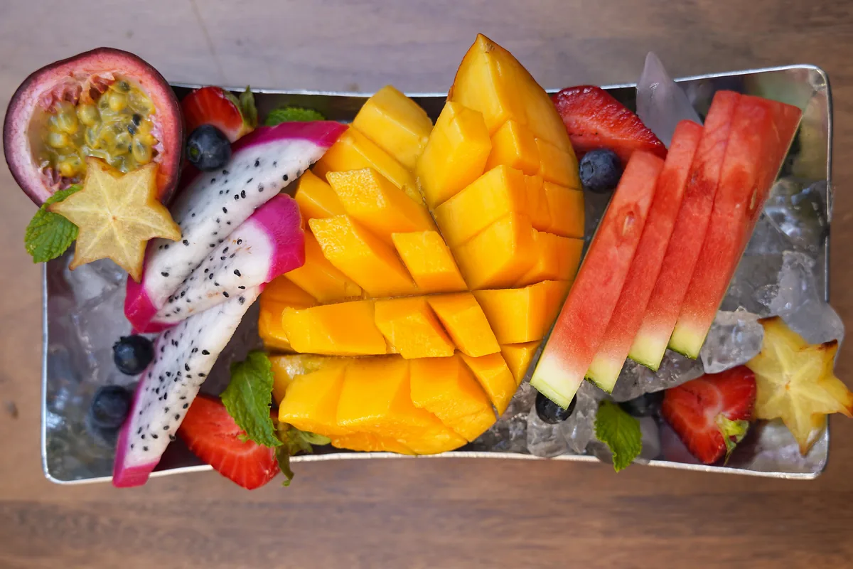 Bandeja Phonlamai vista desde arriba con mango en dados, sandía, pitaya, fresas, arándanos, carambola y maracuyá sobre hielo picado