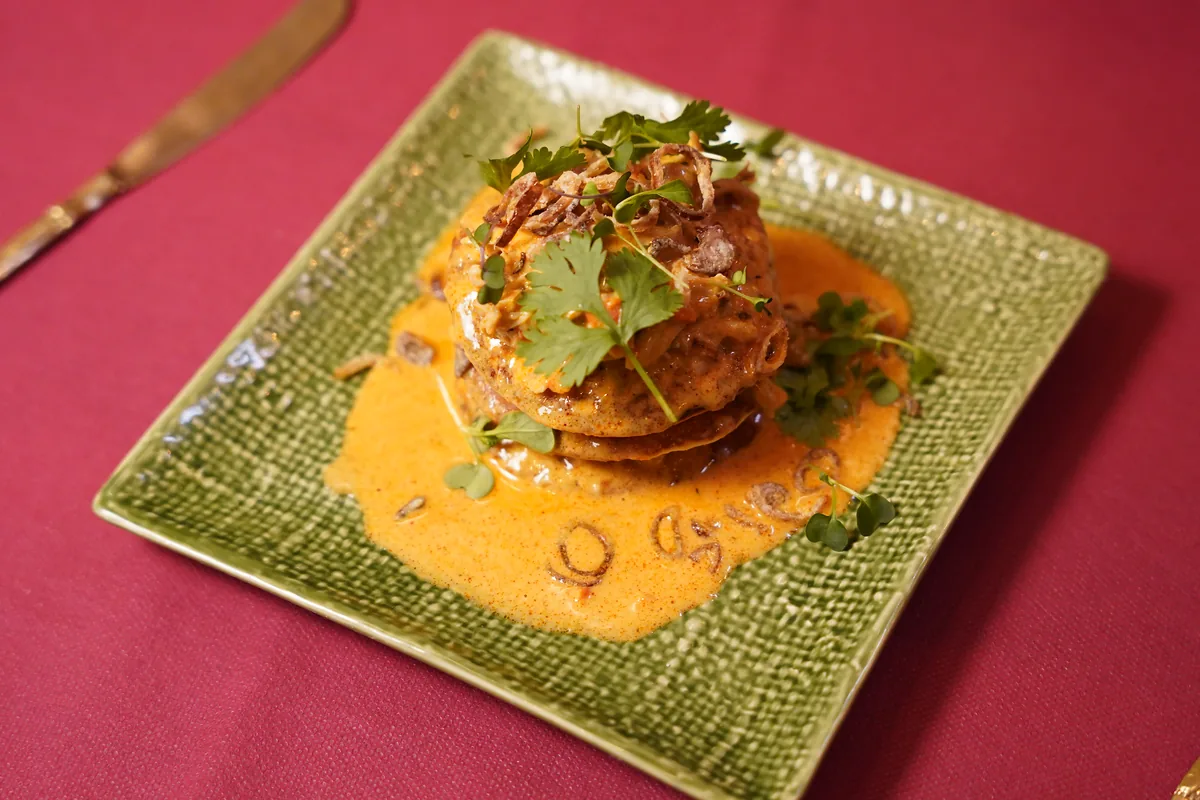 Pancakes tailandeses apilados con curry massaman, pollo desmenuzado, cebolla frita y cilantro en un plato verde